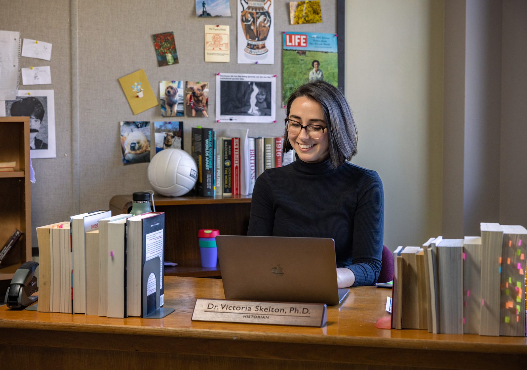 Dr. Victoria Skelton sitting at a desk with books and typing on their laptop