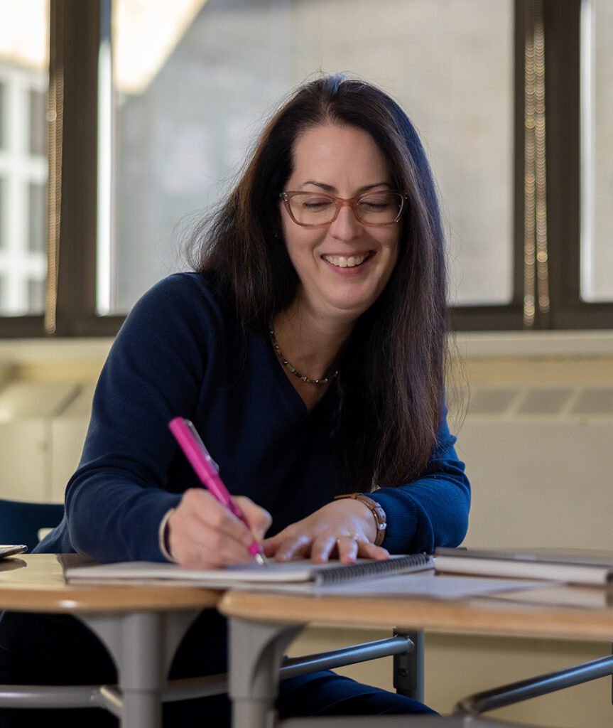 Teacher writing in a notebook while sitting at a desk
