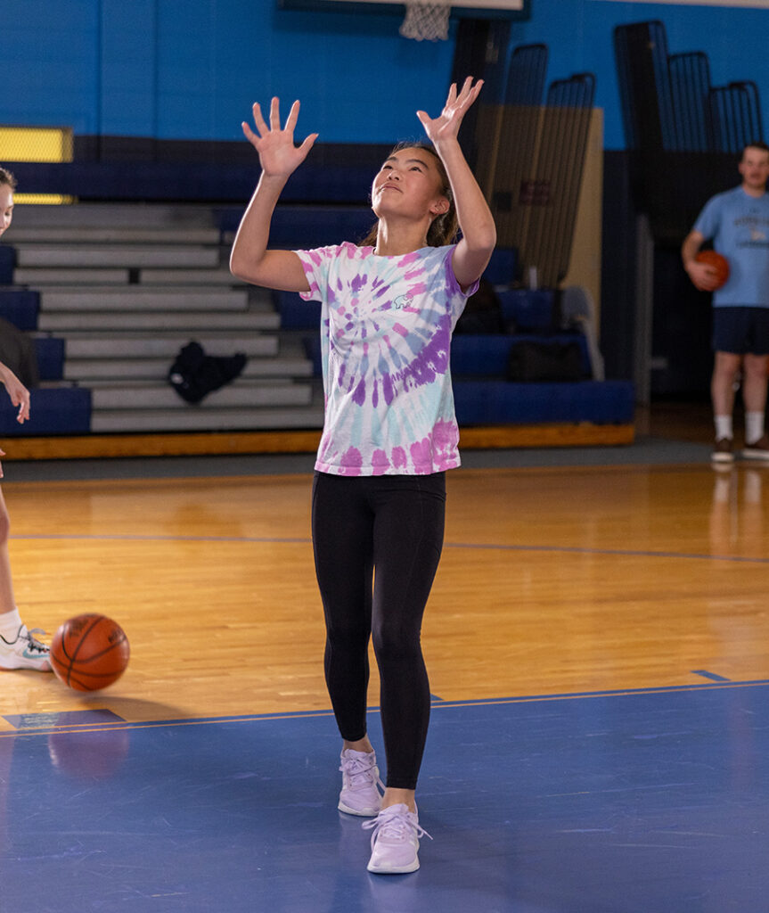 Student athlete inside a gymnasium with a basketball on the ground and both hands held up