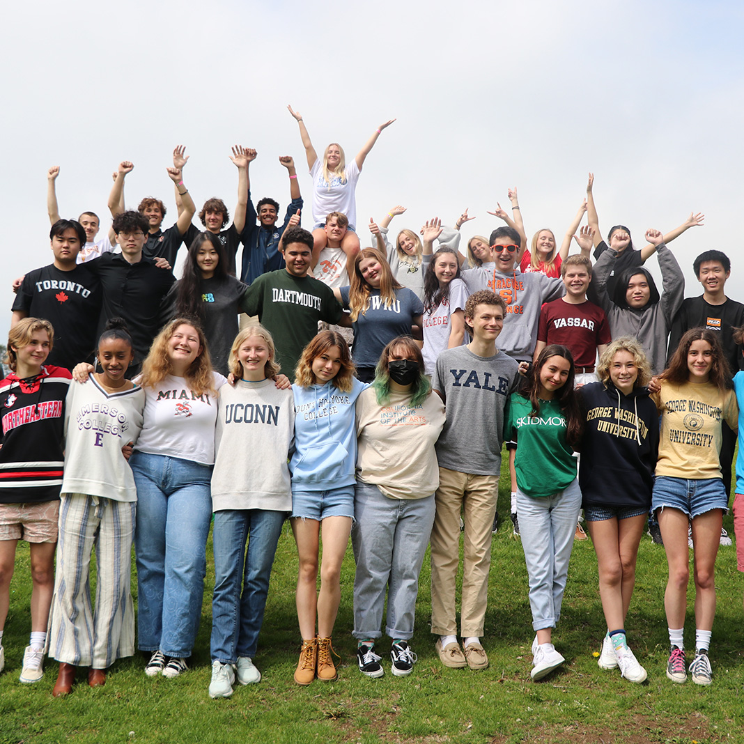 Students wearing different college shirts and sweatshirts and standing close together outside