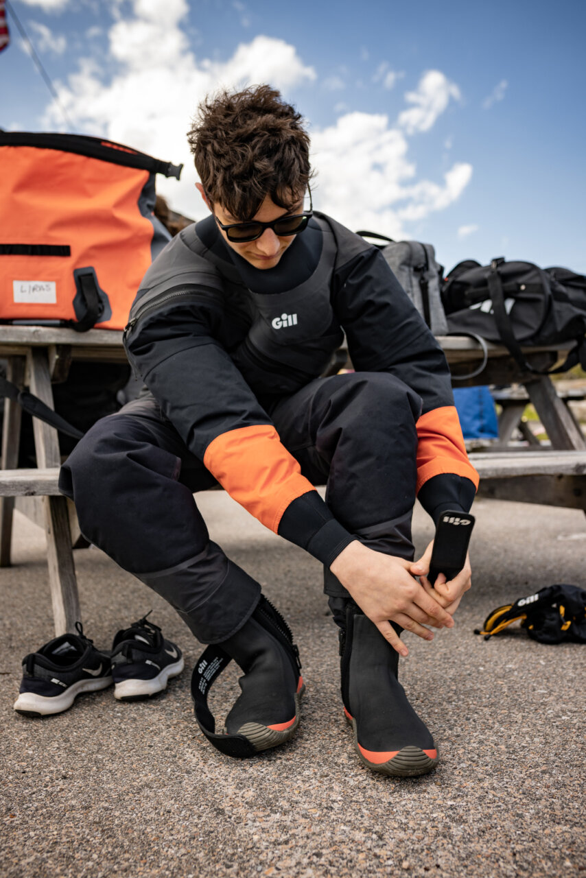 Williams sailing student puts on water gear while sitting at a picnic table