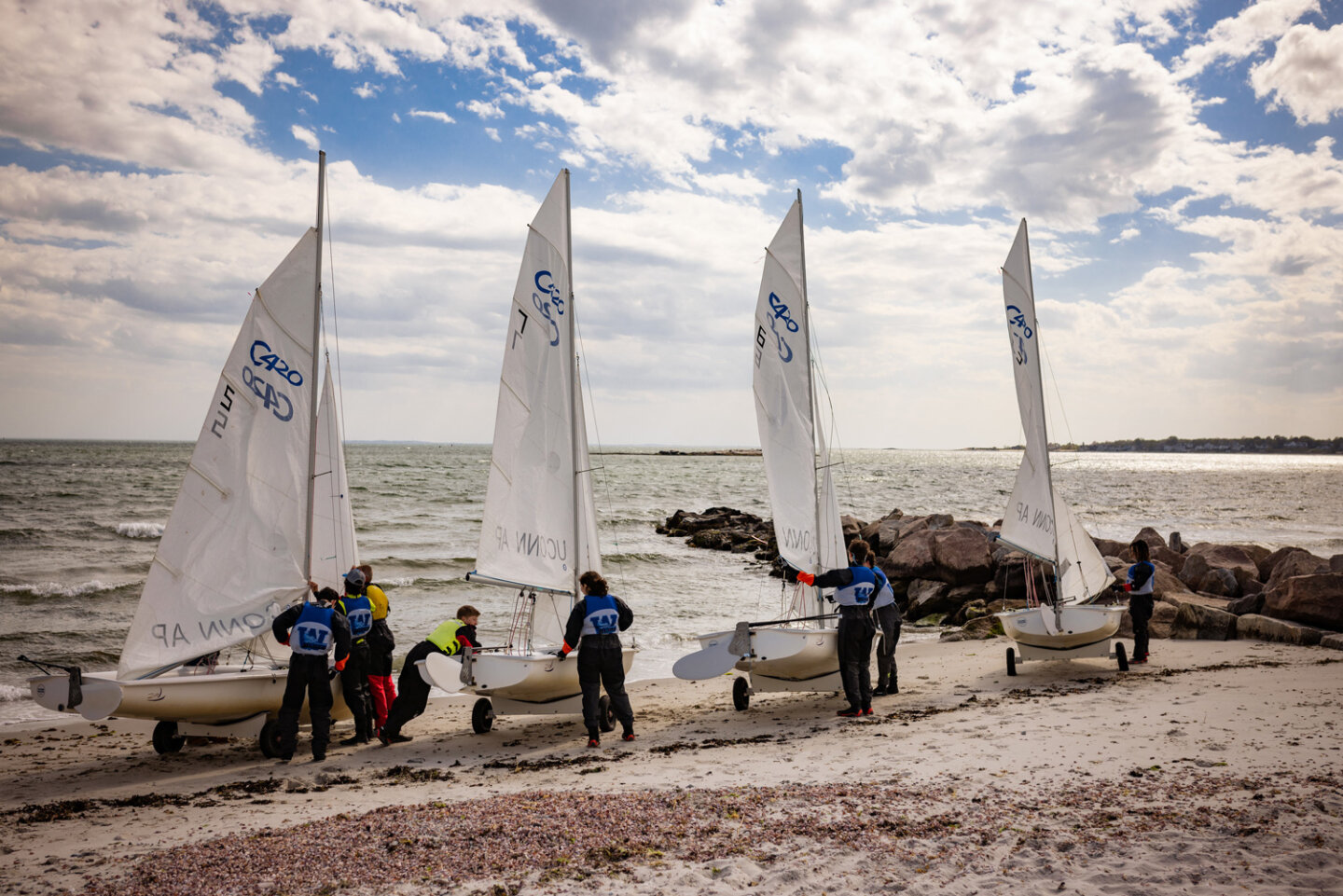 Williams school sailing students line up their sailboats on the beach to launch