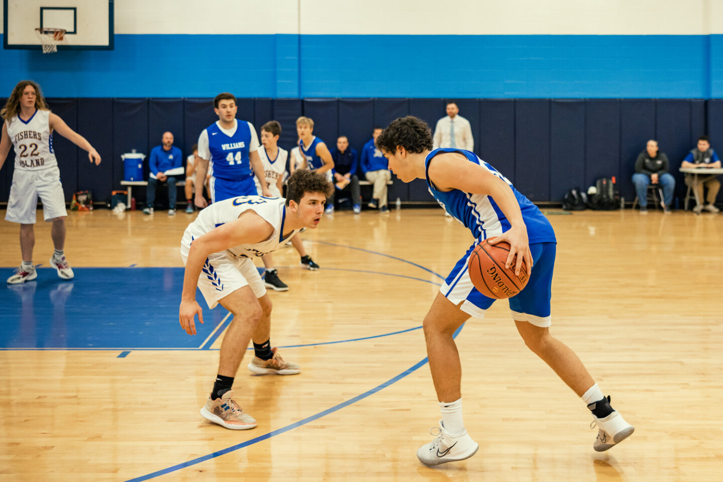 Boys basketball player dribbles toward the basket from the free throw line with defending player crouched