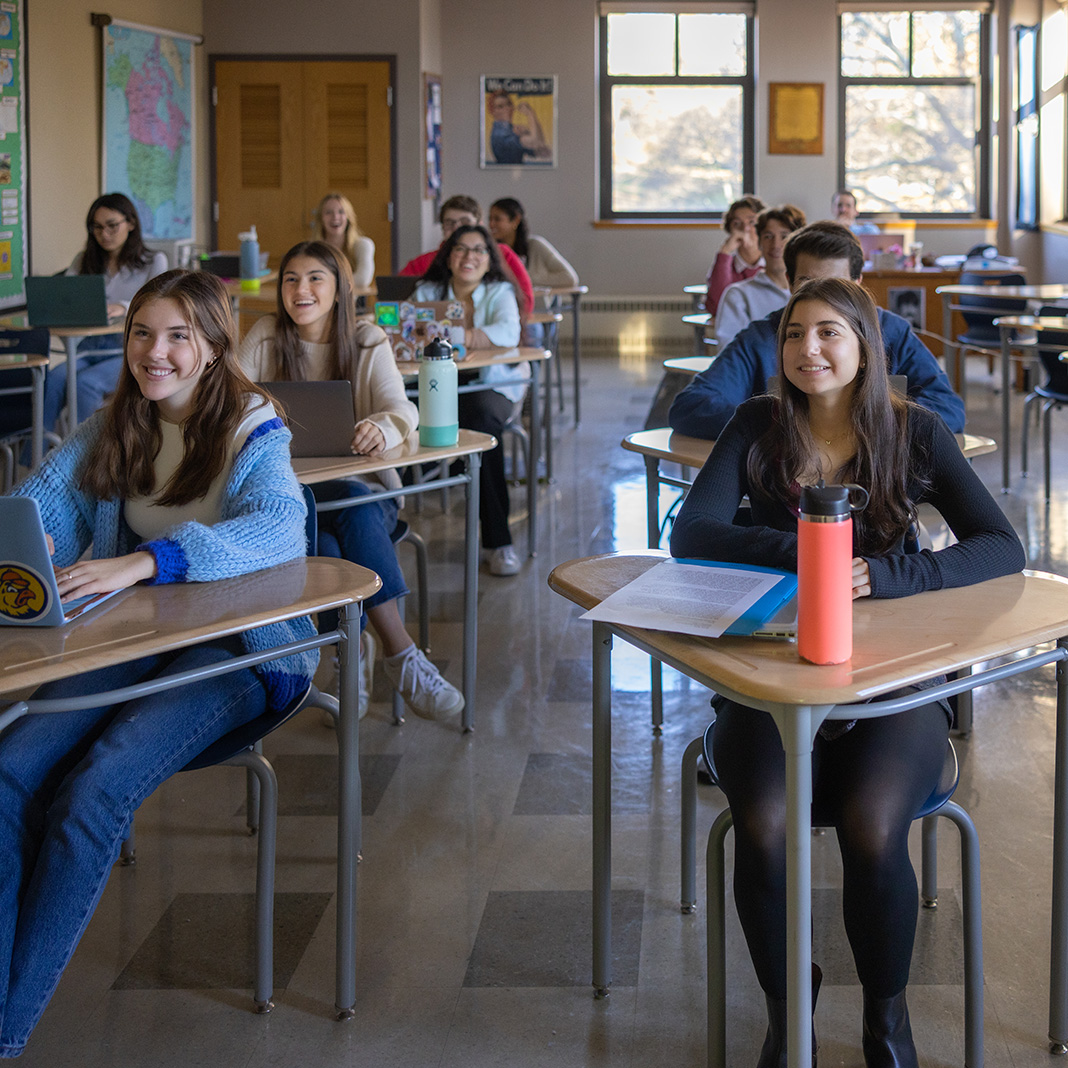 Students sitting in desks looking towards front of classroom and smiling