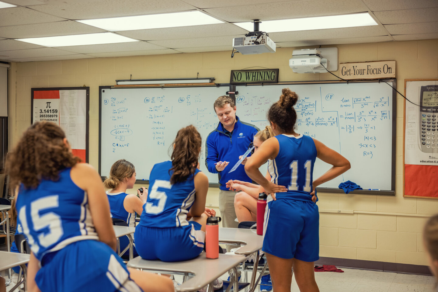 Girls basketball team discusses strategy with basketball coach in math classroom