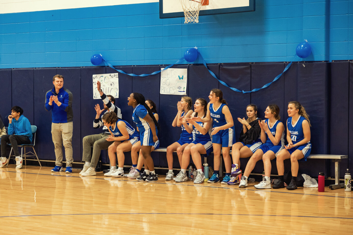 Girls basketball team cheer their teammates from the sidelines with the coach during a game