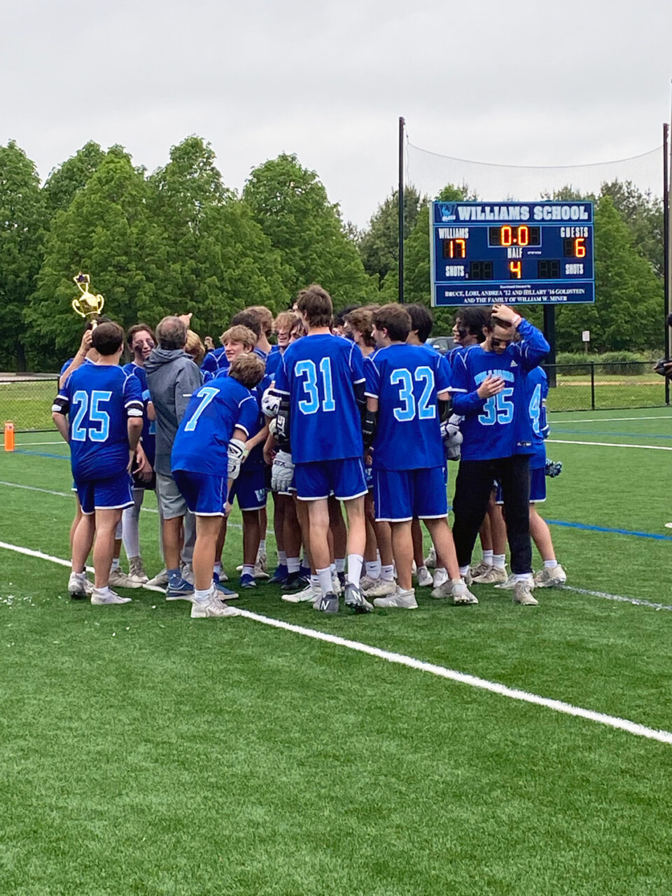 Williams School boys lacrosse team celebrates win in huddle with trophy