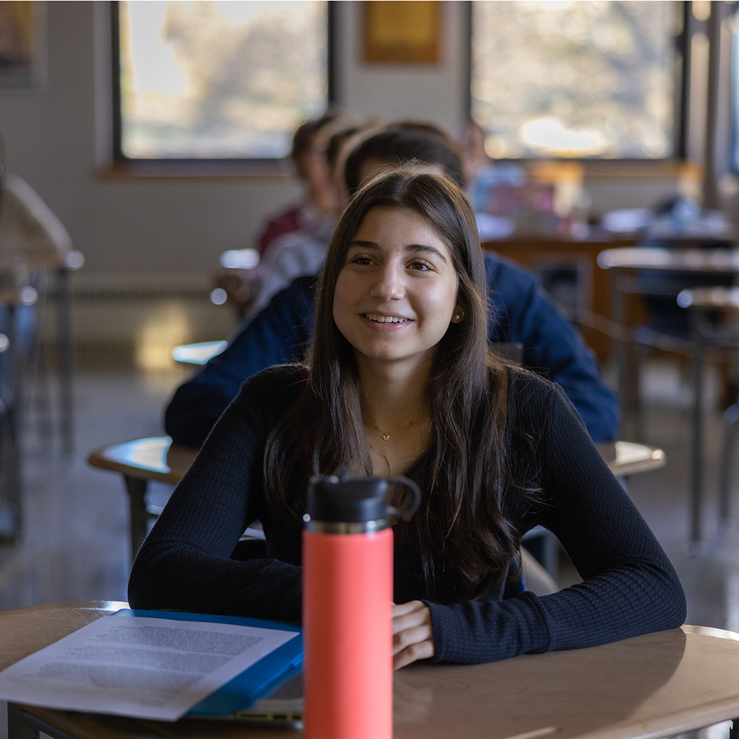 Williams School student smiles at their desk with a bright reusable water bottle on their desk