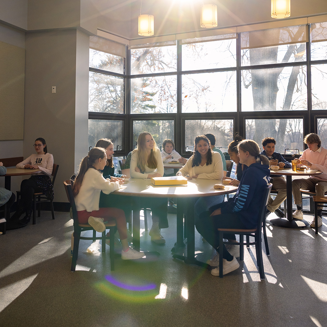 Williams School students at lunch in the cafeteria with sun-filled windows in background