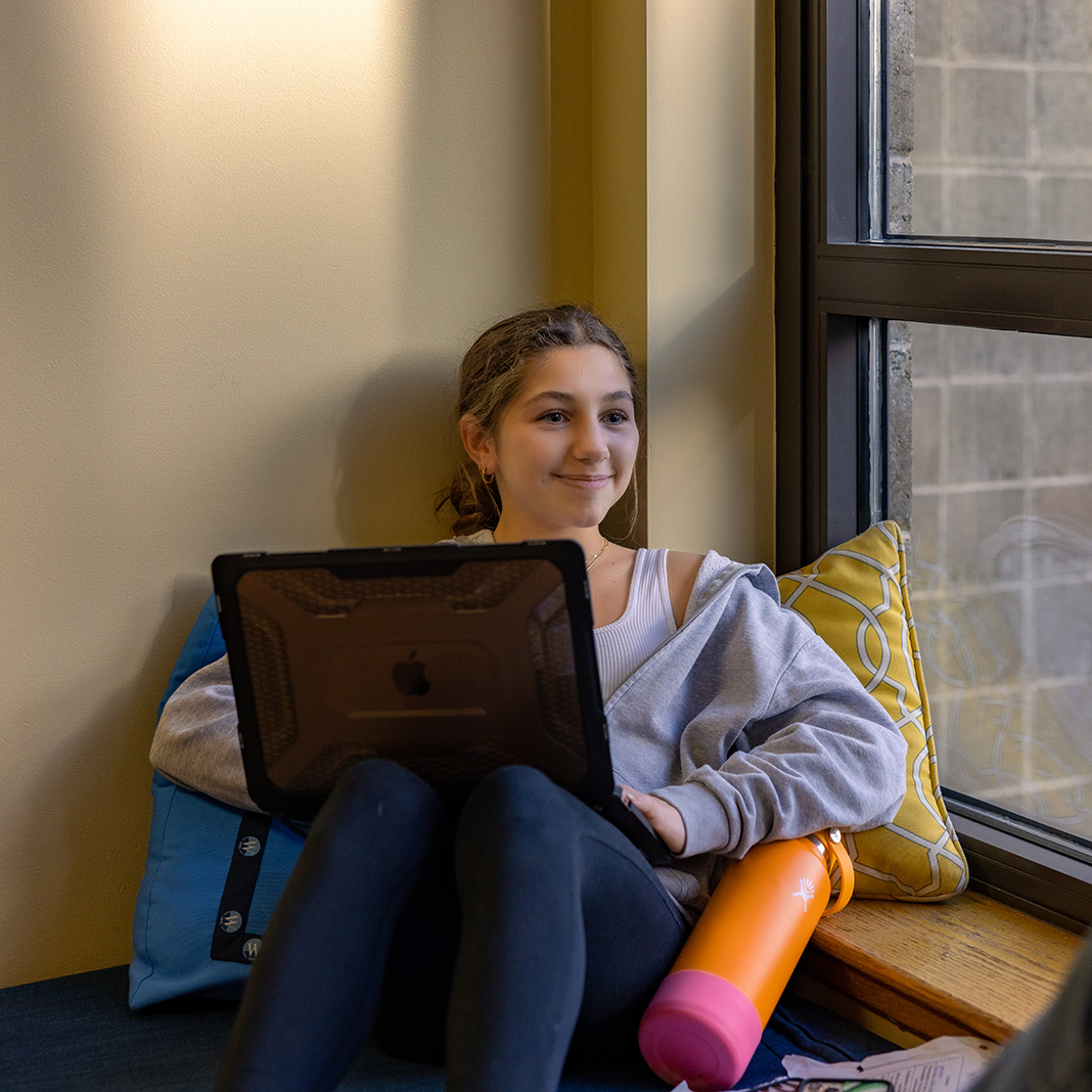 Prospective Williams student sits near the window with a laptop and an orange hydroflask water bottle