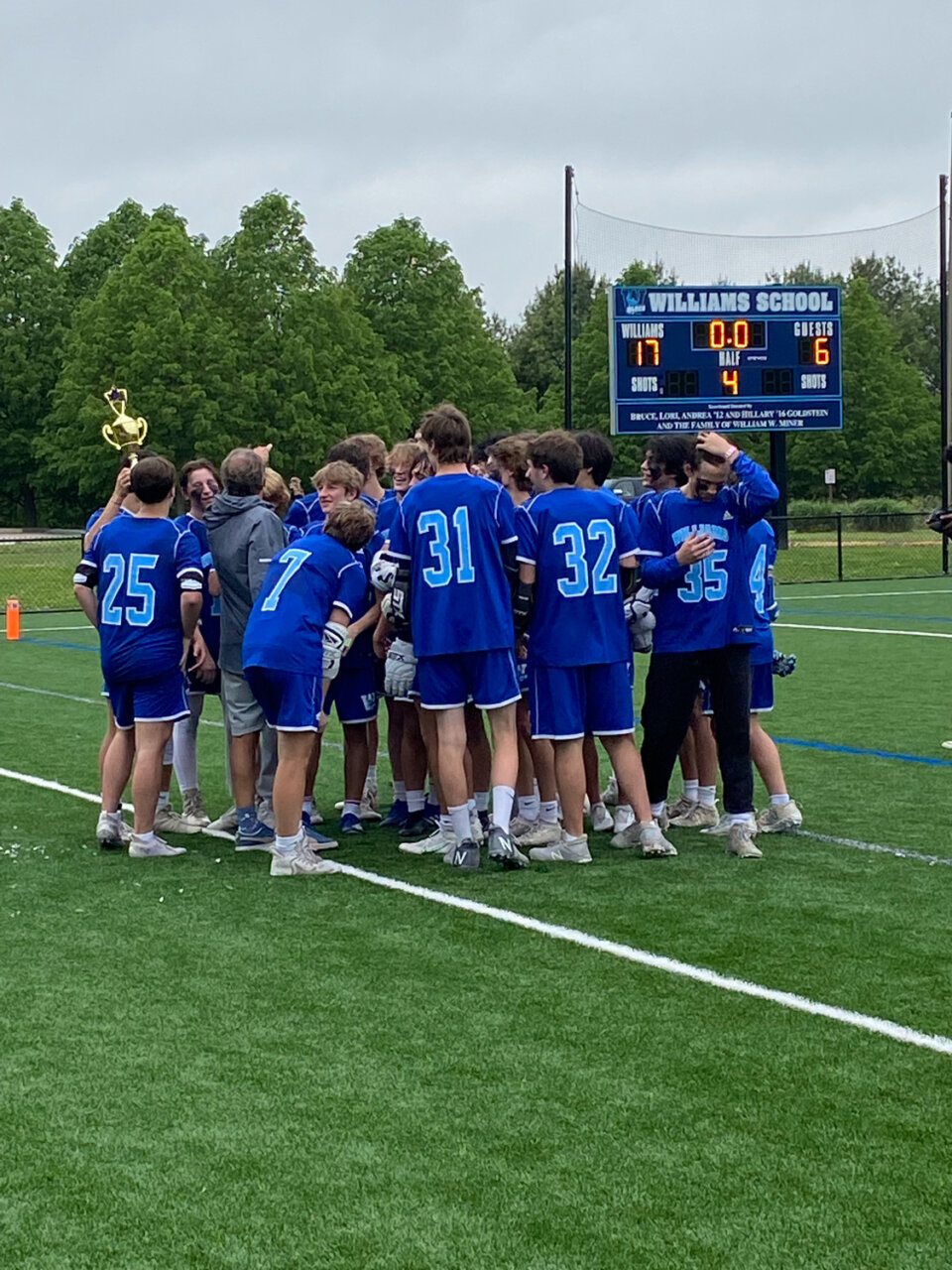 Williams School boys varsity lacrosse HVAL championship game players huddle around celebrating with a trophy