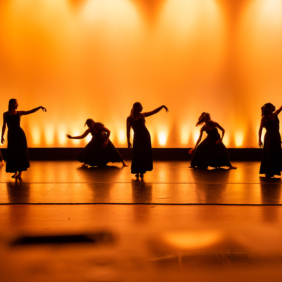 Williams dance students perform on stage with yellow backlighting